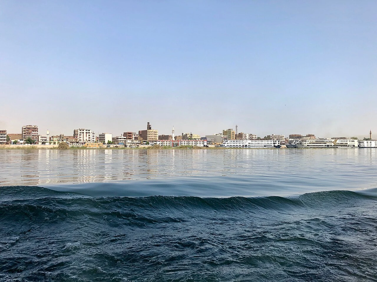 Edfu buildings seen beyond the Nile and a passing wake